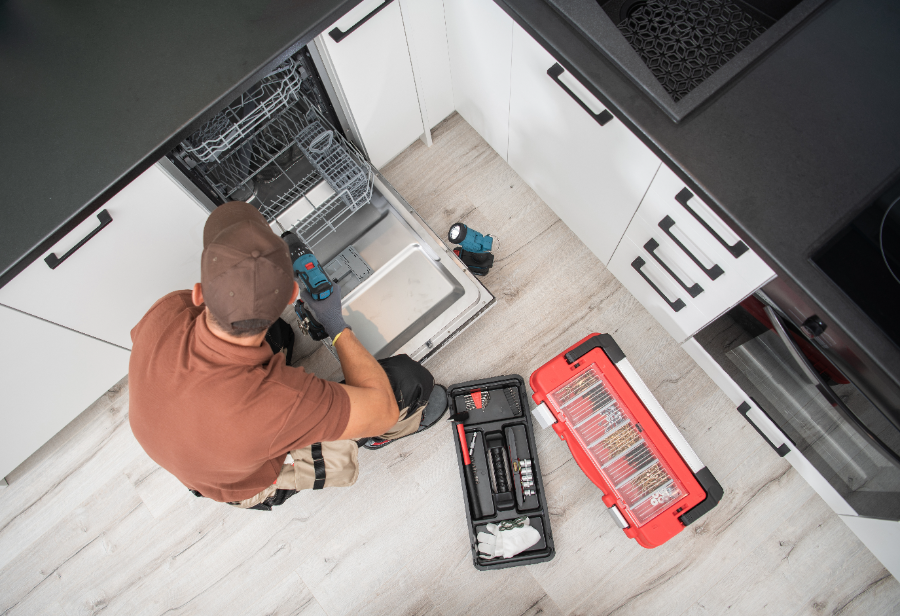 Technician installing dishwasher in kitchen from overhead view with tools on floor