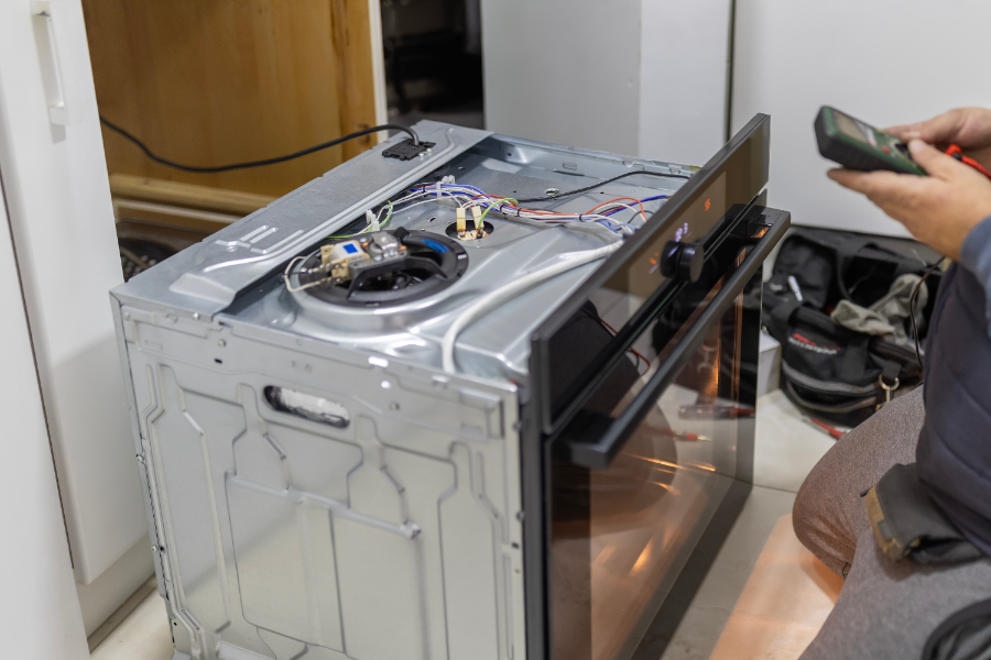 Technician servicing interior components of a white dishwasher with exposed heating element and wiring