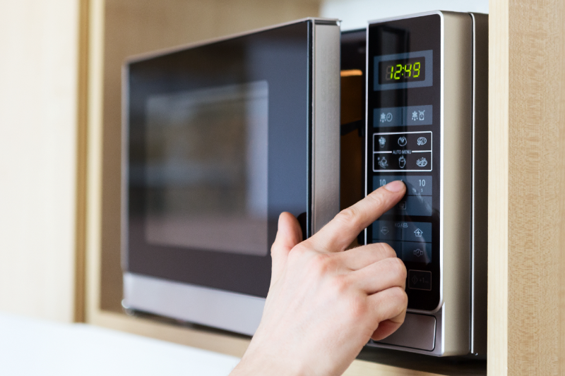 Person's hand pressing button on microwave oven control panel displaying 12:49