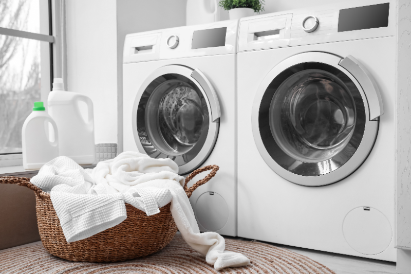 Modern laundry room with two white washing machines, basket of white clothes, and detergent bottles