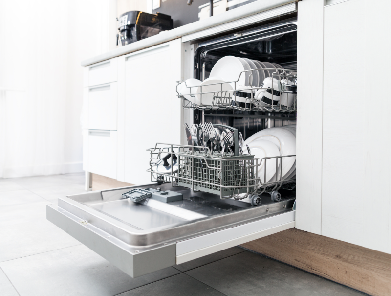 Open dishwasher with clean dishes in racks in modern white kitchen