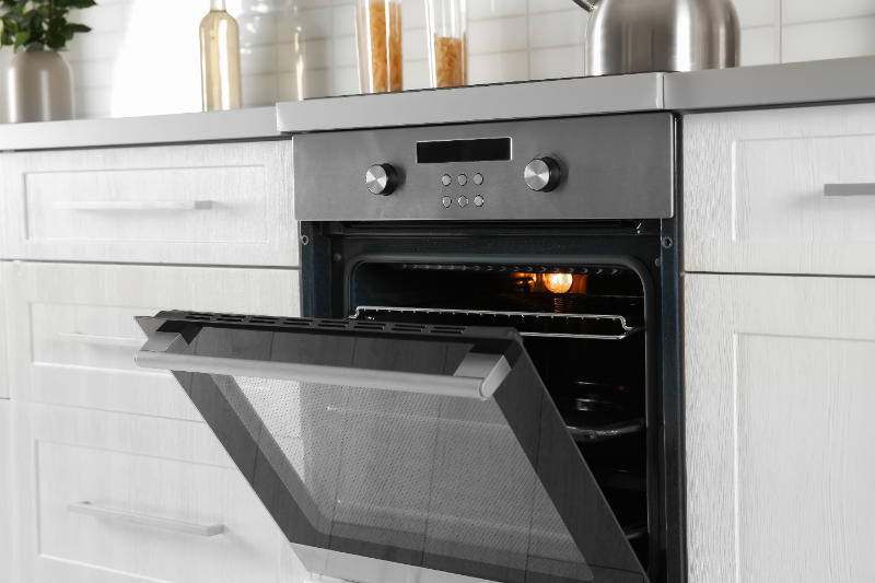 Built-in stainless steel oven with open door in modern white kitchen cabinet